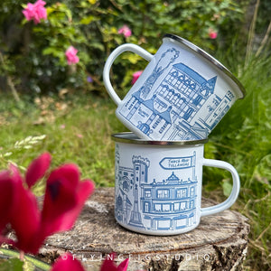 An enamel mug featuring detailed illustrations of various buildings and landmarks in Tullamore, including the Tullamore Dew Distillery and Charleville Castle. The mug has a white enamel finish with a silver rim. It is designed, illustrated, and hand-printed in Offaly. The mug is lightweight yet sturdy, making it ideal for camping, picnics, or enjoying a cosy morning at home. Each mug is hand printed and packaged in plastic-free and recyclable materials.